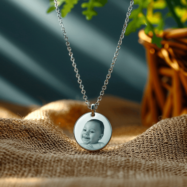 Silver necklace featuring a gravure photo of a smiling baby, set against a natural backdrop.