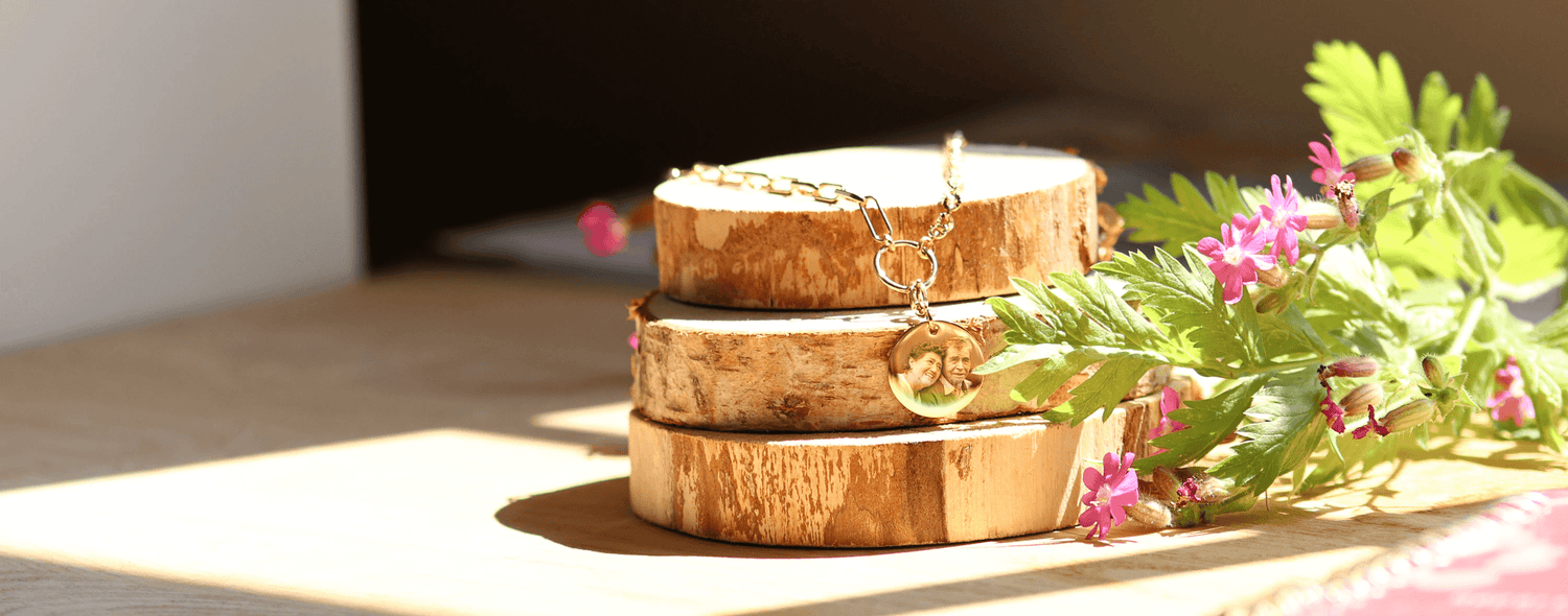 Pendentif gravé sur des rondins de bois, orné de fleurs, illuminé par la lumière naturelle, symbolisant élégance et durabilité.