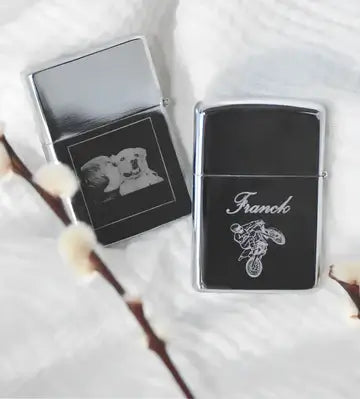 Briquets Zippo gravés, l'un avec un chien, l'autre portant le nom Franck, sur fond doux et texturé.