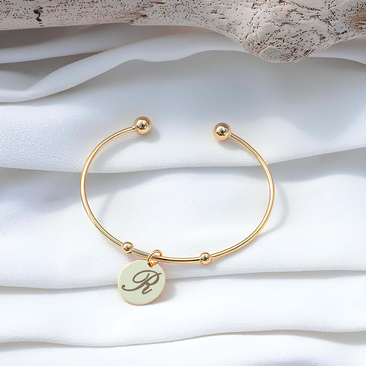 Bracelet personnalisé en or avec gravure de la lettre R, élégant et minimaliste sur fond de tissu doux.
