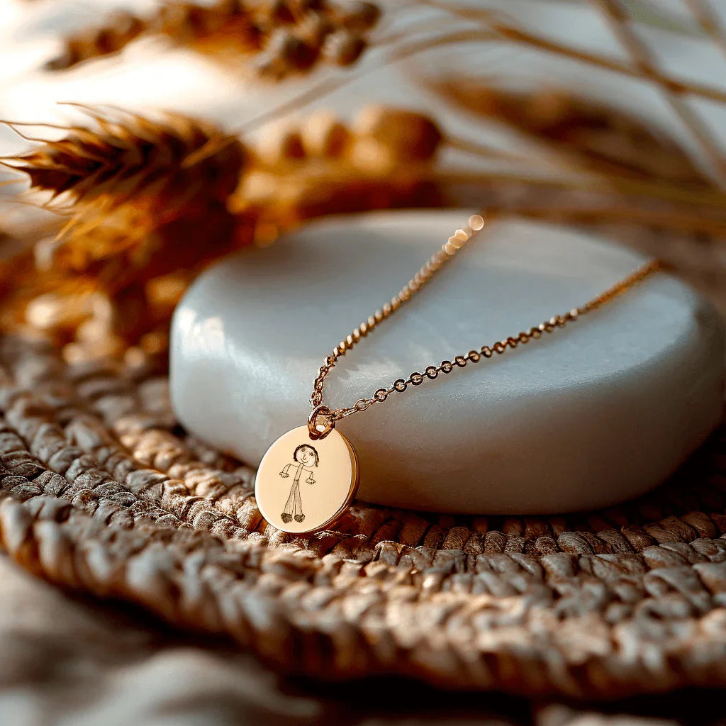 Medium round medallion in gilded steel with engraving, on a delicate chain, placed on a natural support.