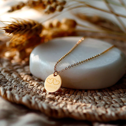 Moyen médaillon rond gravé en acier doré avec motif cœur et date, posé sur un support en pierre.