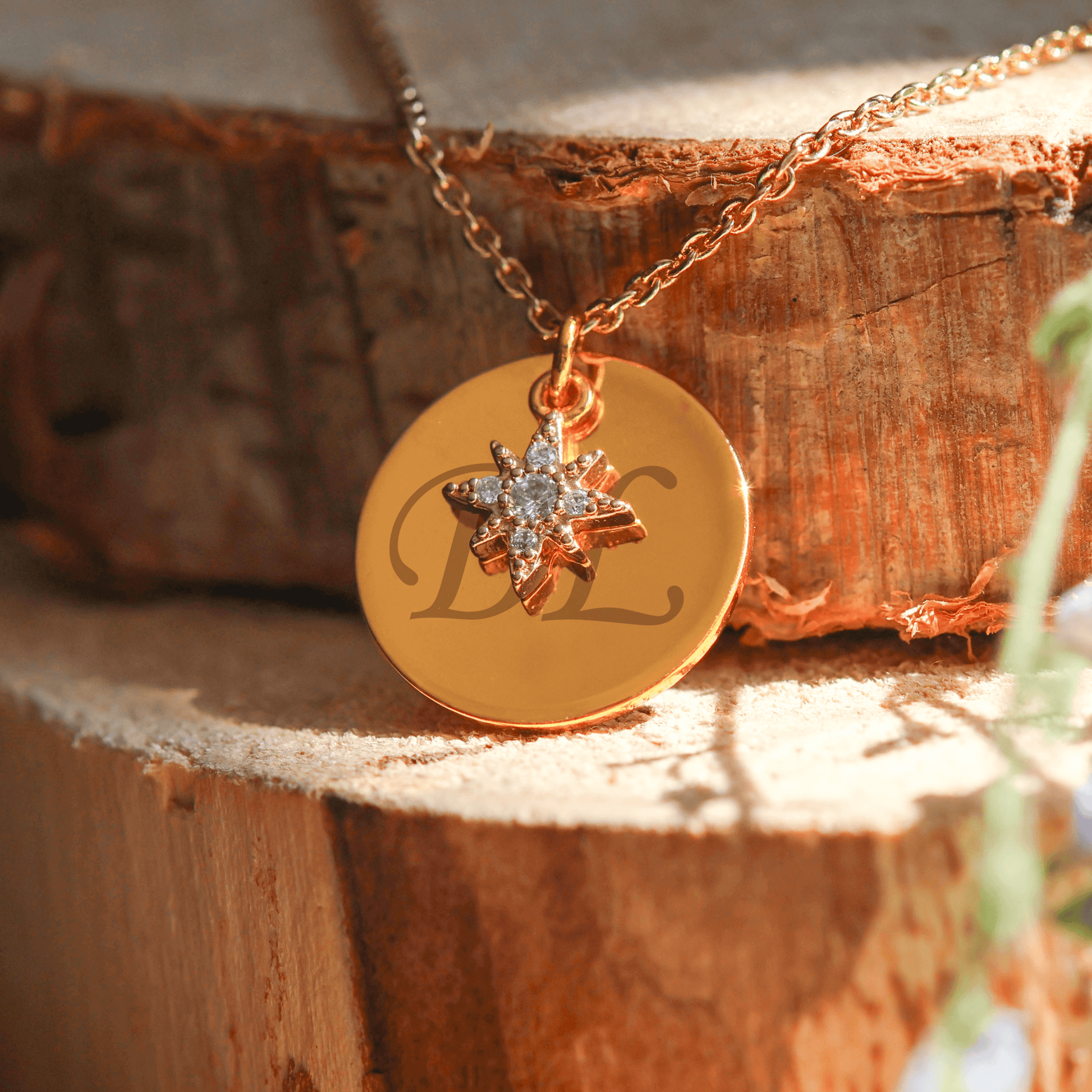 Collier plaqué or avec pendentif étoile en cristal et médaillon personnalisable, sur fond bois.