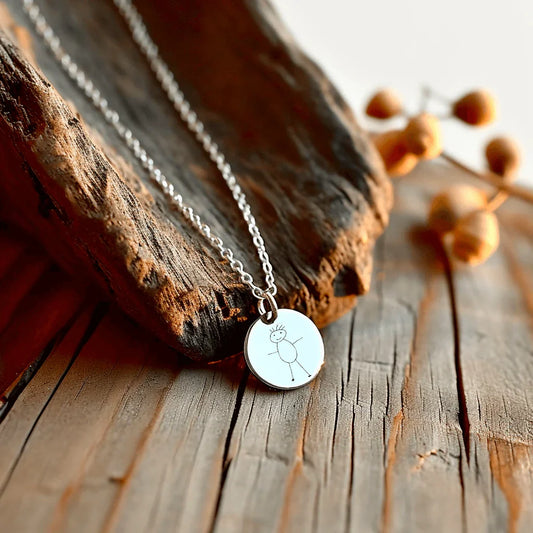 Médaillon rond en acier argenté gravé avec un dessin unique, suspendu à une chaîne sur un fond en bois.