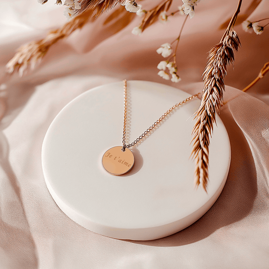 Pendentif gravé en acier doré sur un support, avec inscription 'Je t'aime' et décor floral.
