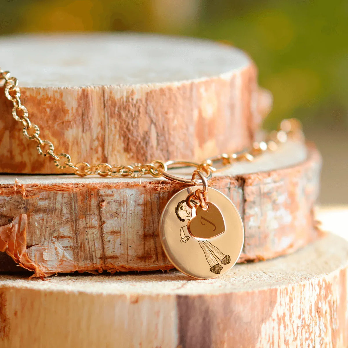 Collier rond plaqué or gravé avec un dessin d'enfant, sur un support en bois, symbole de souvenirs précieux.