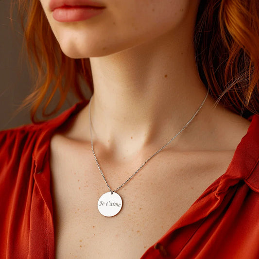 Pendentif gravé en acier argenté avec le texte 'Je t'aime', porté par une femme avec une blouse rouge.
