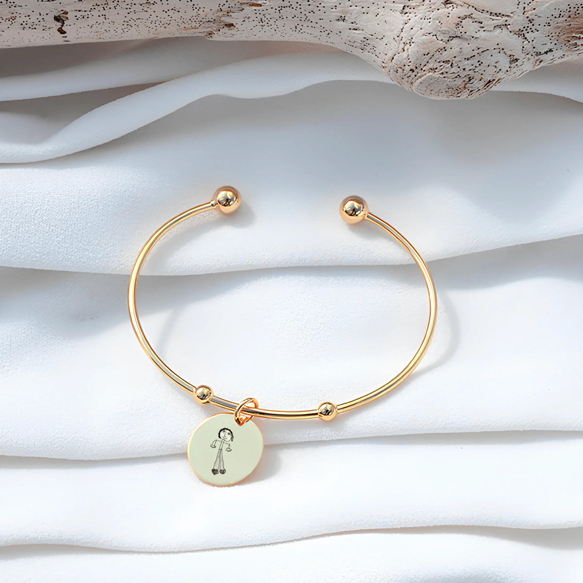 Bracelet jonc doré avec pendentif rond gravé, personnalisé GravurePhoto, posé sur tissu blanc.