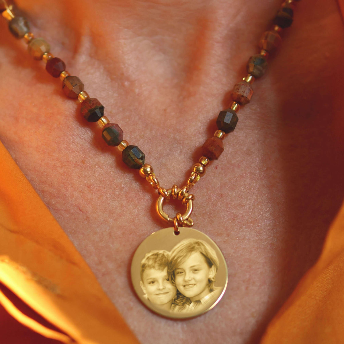 Necklace with engraved pendant, warm colored beads on orange blouse.