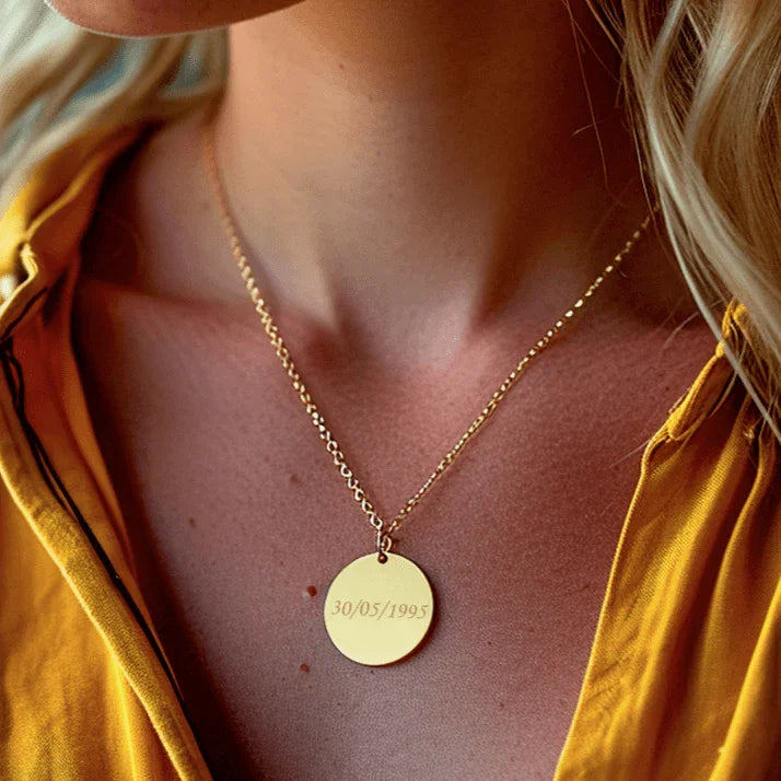 Personalized round gold steel pendant with date engraving, worn by a woman in a yellow top.