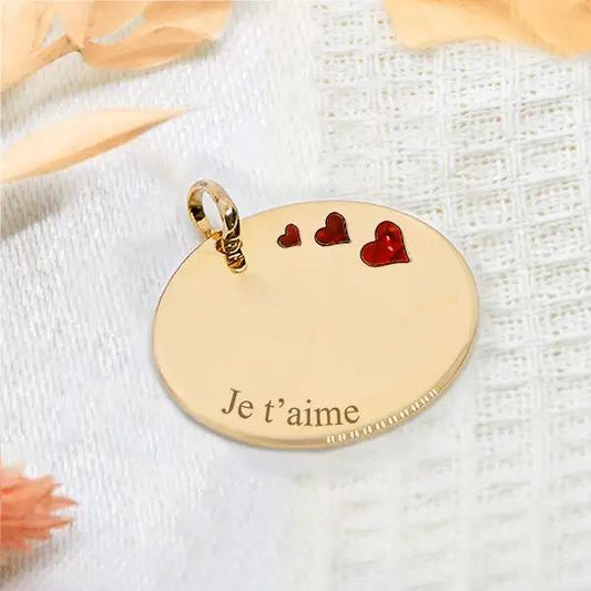 Médaillon rond en plaqué or orné de 3 cœurs rouges et gravé "Je t'aime", diamètre 2,5 cm.